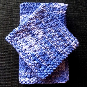 May include: Folded blue and white knitted washcloth. The washcloth is made of a soft, textured yarn, with a pattern of alternating blue and white sections. The washcloth is folded in a way that shows off the texture and color variations.