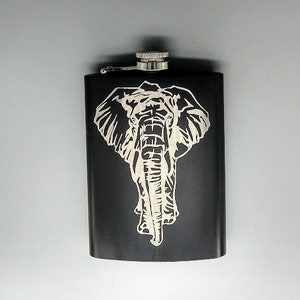 Puede incluir: Una petaca de acero inoxidable negra con un diseño de elefante plateado grabado en la parte delantera.