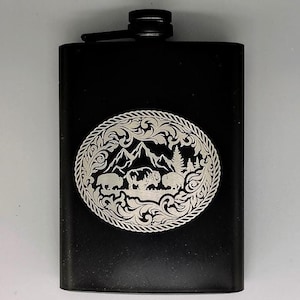 May include: Black metal flask with a silver engraved design of a mountain scene with trees and animals. The design is surrounded by a rope-like border.
