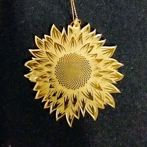 May include: A gold-colored metal ornament shaped like a sunflower. The ornament has a detailed design with a central circle and petals.