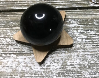 May include: A black obsidian sphere on a wooden star-shaped stand. The sphere is smooth and polished, reflecting light.