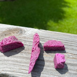 May include: Four pieces of purple sponge candy on a wooden surface. The candy is irregular in shape and has a porous texture.