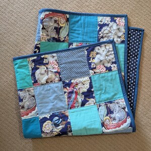 May include: Two patchwork quilts with a variety of fabrics. One quilt features a navy blue border with white stars. The other quilts have a teal border. The patchwork includes koalas, birds, and floral patterns in shades of blue, teal, and white.