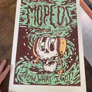 Puede incluir: Una ilustración verde y marrón de una calavera con casco con el texto "Mopeds are everywhere. Now what I got!"