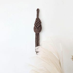 以下が含まれることがあります： 涙の形をした茶色のマクラメの壁掛けで、下部にフリンジが付いています。