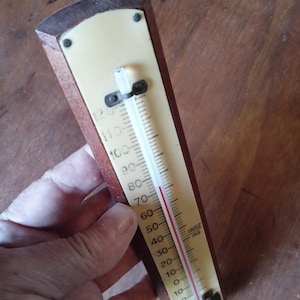 Puede incluir: Un termómetro de pared vintage con un marco de madera marrón oscuro y una esfera de color crema. La escala muestra temperaturas de -20 a 120 grados Fahrenheit, con la palabra FREEZING impresa claramente junto a la marca de 32 grados.