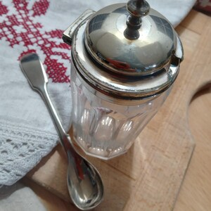 Senapskruka i slipat glas med gångjärnsförsett lock och försilvrad sked, 1920-talet. 12 cm.