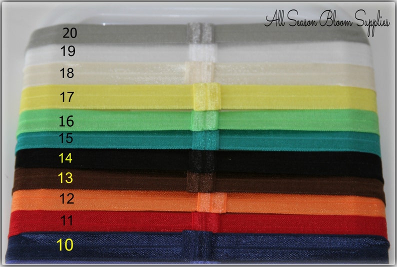 Pu&ograve; includere: Un set di 10 elastici per capelli di diversi colori, numerati da 10 a 20. Gli elastici sono disposti in una pila verticale, con il colore pi&ugrave; scuro in basso e il colore pi&ugrave; chiaro in alto. Il testo "All Season Bloom Supplies" &egrave; visibile nella parte superiore dell'immagine.