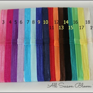 Pu&ograve; includere: Venti elastici per capelli di colori assortiti, numerati da 1 a 20. Gli elastici per capelli sono disposti in fila su una superficie bianca. All Season Bloom Supplies &egrave; scritto in corsivo nella parte inferiore dell'immagine.