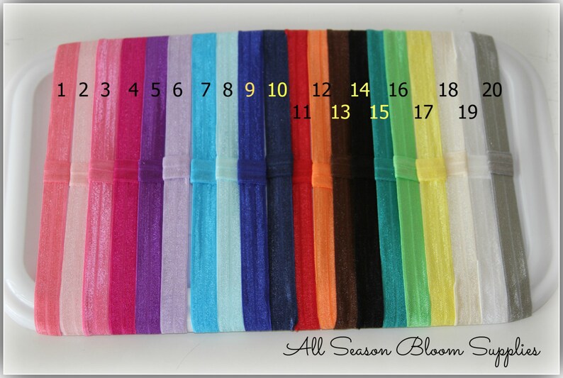 Pu&ograve; includere: Venti elastici per capelli di colori assortiti, numerati da 1 a 20. Gli elastici per capelli sono disposti in fila su una superficie bianca. All Season Bloom Supplies &egrave; scritto in corsivo nella parte inferiore dell'immagine.
