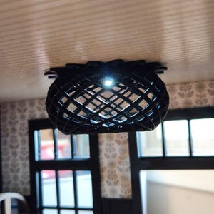 May include: A black, spherical, lattice-patterned ceiling light fixture mounted to a flat surface. The structure features a grid-like design with an illuminated center point, casting light through the open geometric gaps of the dark frame.