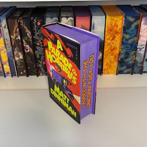 May include: A hardback book titled "A Parade of Horribles" by Matt Dinniman. The book has a purple spine with the text "I AGREE WITH THE UNICORN. FUCK YOU." The cover features a red and black design with a purple vehicle.