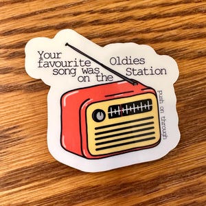 Puede incluir: Una pegatina blanca con una ilustración de una radio vintage roja y amarilla. El texto en la pegatina dice "Your favourite song was on the Oldies Station push on through".