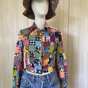 May include: A colourful patchwork button-up shirt with long sleeves. The shirt is made of different fabrics and patterns, including floral, geometric, and paisley. The shirt is cropped and has a relaxed fit.