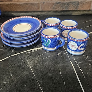 May include: A set of ceramic espresso cups and saucers featuring a hand-painted blue and white design. The cups display fish motifs and red dotted rims, while the saucers have concentric blue rings and matching red dotted edges on the borders.
