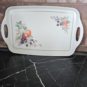 May include: A rectangular off-white serving tray with integrated side handles, featuring a decorative botanical illustration of colorful fruits, including pears, peaches, grapes, and blackberries, arranged in two corners of the central surface.