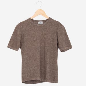 May include: A short-sleeved brown knit top hangs on a wooden hanger. The top has a crew neck and a textured appearance. A small label is visible near the neckline. The garment is displayed against a plain white background.