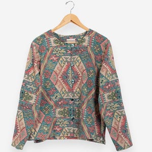 May include: A button-down jacket with a geometric pattern in shades of teal, pink, and beige. The jacket is hanging on a wooden hanger. The pattern features diamond and rectangular shapes.
