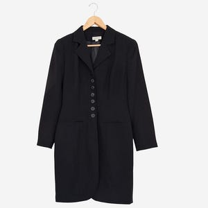 Peut inclure: Une robe blazer noire à manches longues et à boutons sur le devant. La robe est suspendue à un cintre en bois sur fond blanc. La robe a une coupe ajustée et un ourlet au genou.