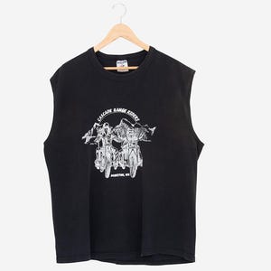 Op de afbeelding: Zwart mouwloos T-shirt met een witte afbeelding van twee motorfietsen en de tekst "CASCADE RANGE RIDERS, MORTON, WA". Het T-shirt hangt aan een houten hanger.