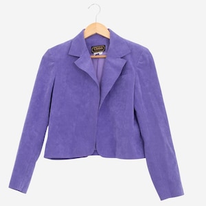 May include: A lavender blazer with a notched lapel and long sleeves hangs on a wooden hanger. The blazer has a single-button closure and a small pocket on the left side. The brand name "Clarion" is visible on a tag.