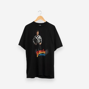 May include: Black t-shirt with a graphic print of a man wearing a checkered shirt and the text "Donnie McCaslin" in colorful letters.