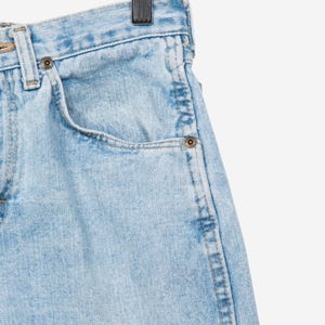 May include: Light blue denim jeans featuring a high-waisted design with a classic five-pocket construction, metal rivets, a button fly closure, and visible stitching details, suspended from a wooden hanger by a metal clip.