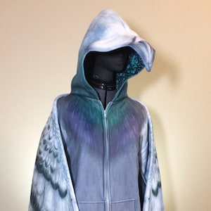 Puede incluir: Una sudadera con capucha gris con cierre de cremallera y alas adjuntas. Las alas est&aacute;n impresas con un patr&oacute;n de plumas realista en tonos grises y azules.