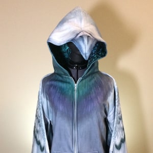 Puede incluir: Una sudadera con capucha azul y gris con cierre de cremallera y mangas largas. Las mangas est&aacute;n dise&ntilde;adas para parecer alas con un patr&oacute;n de plumas blancas y grises.