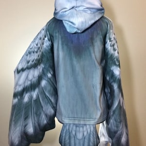 Puede incluir: Una sudadera con capucha azul con un dise&ntilde;o de p&aacute;jaro. Las alas y la cola est&aacute;n impresas en las mangas y la parte inferior de la sudadera.