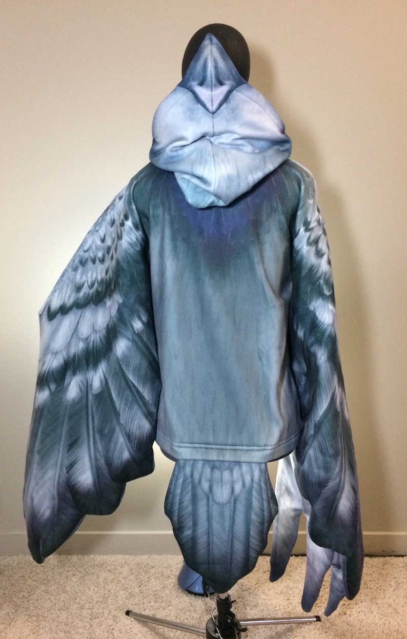 Puede incluir: Una sudadera con capucha azul con un dise&ntilde;o de p&aacute;jaro. Las alas y la cola est&aacute;n impresas en las mangas y la parte inferior de la sudadera.