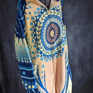 May include: A blue and yellow hooded jumpsuit with a cat face on the hood. The jumpsuit has a mandala pattern on the front and a zipper down the front.