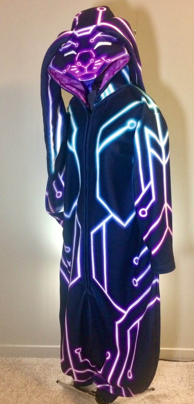 May include: A black hooded jumpsuit with a white and purple circuit board design. The hood has a bunny rabbit face with glowing eyes.