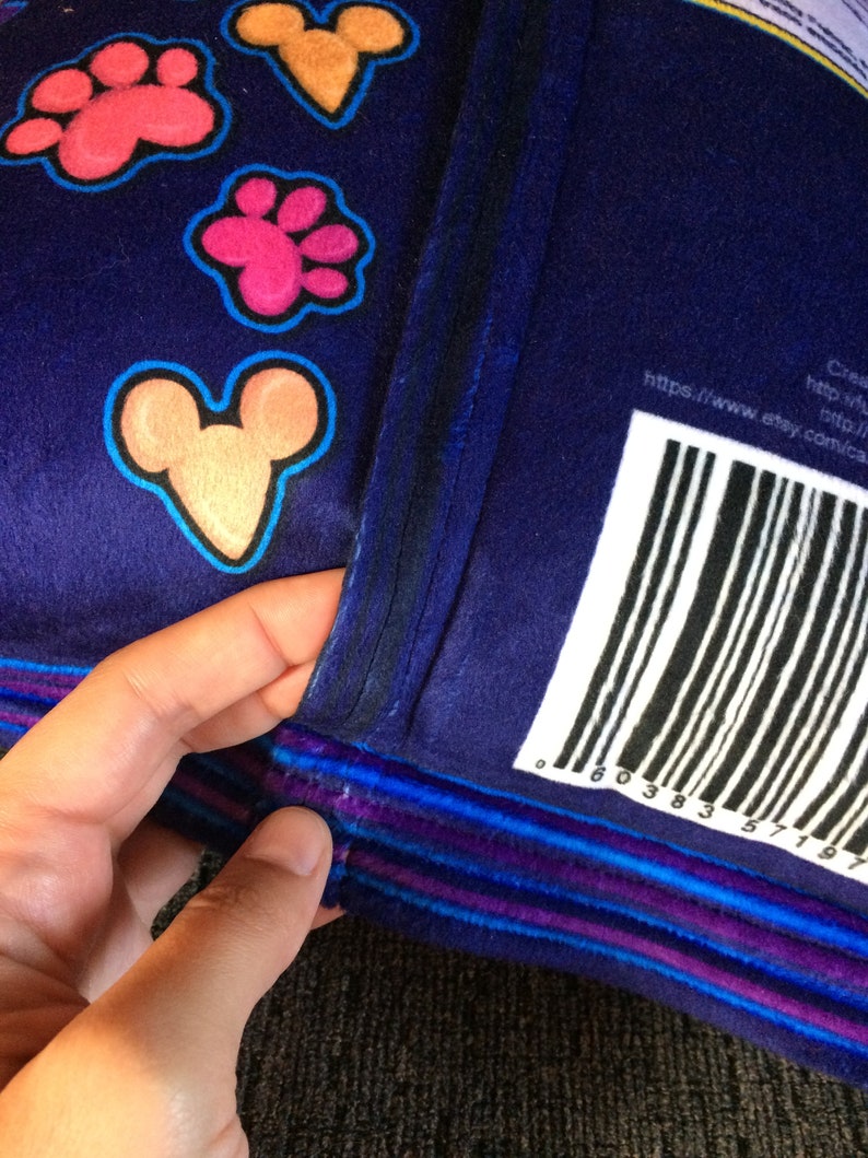 May include: A blue plush pillow with a colorful paw print and Mickey Mouse design. The pillow has a purple, blue, and white striped trim. The back of the pillow has a barcode and the text "https://www.etsy.com/ca-en/shop/comical"
