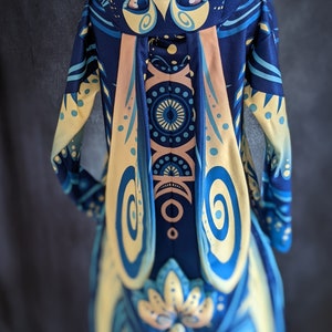 May include: A blue and yellow hooded sweatshirt with a rabbit design. The hood has a rabbit face with large eyes and a pink nose. The sweatshirt has a swirling pattern on the front and back.