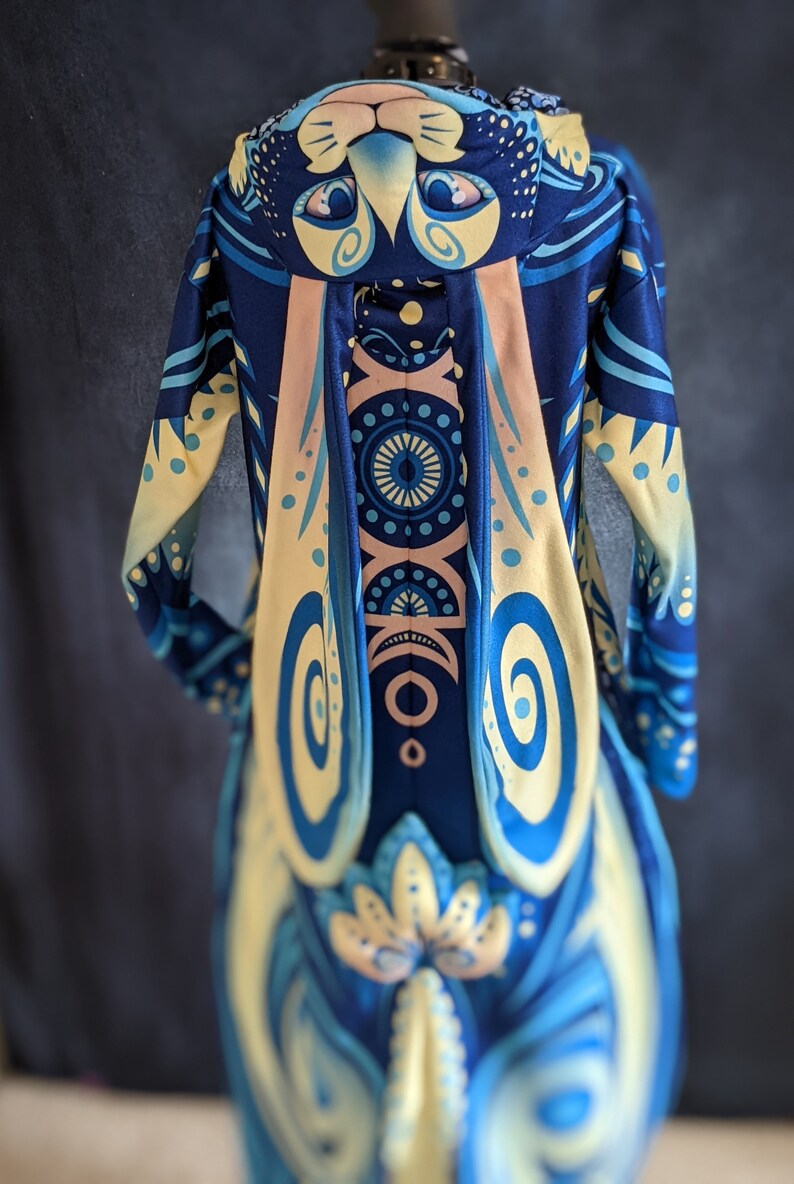 May include: A blue and yellow hooded sweatshirt with a rabbit design. The hood has a rabbit face with large eyes and a pink nose. The sweatshirt has a swirling pattern on the front and back.