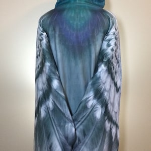 Puede incluir: Una sudadera con capucha azul con un dise&ntilde;o de alas de plumas en las mangas. Las alas son un degradado de azul, blanco y gris.