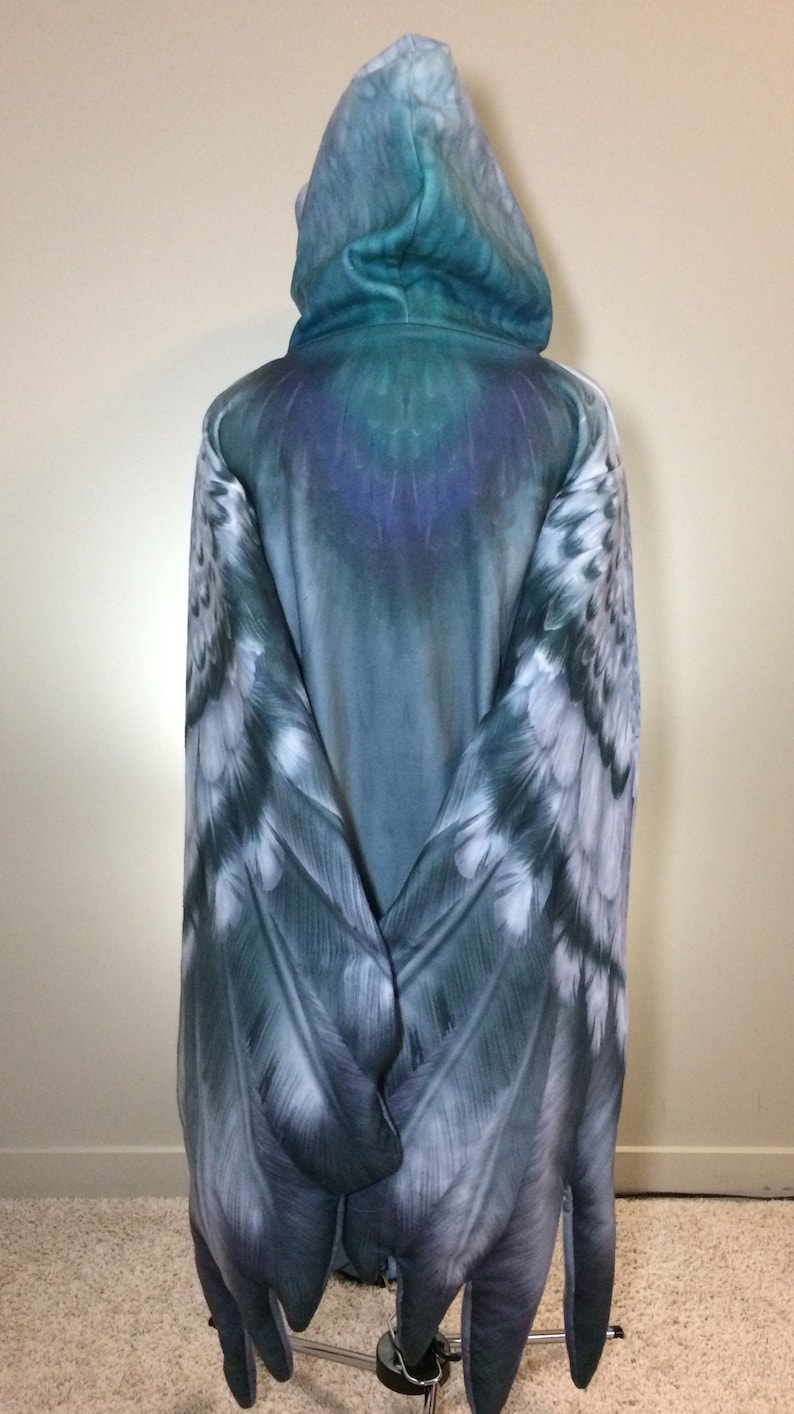 Puede incluir: Una sudadera con capucha azul con un dise&ntilde;o de alas de plumas en las mangas. Las alas son un degradado de azul, blanco y gris.