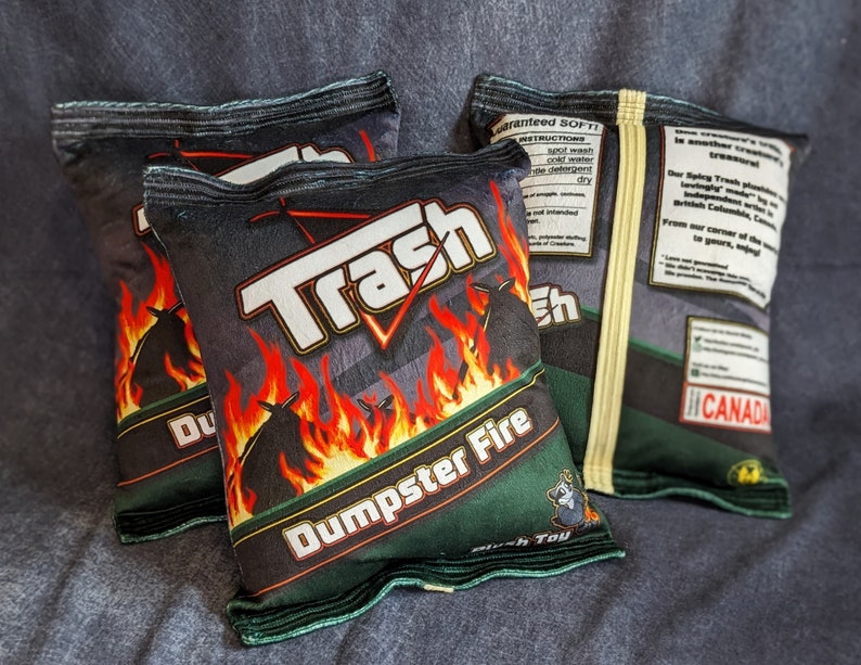 May include: Three black and green chip bags with the words "Trash" and "Dumpster Fire" printed on them. The bags are made of a soft, plush material and are designed to look like real chip bags.