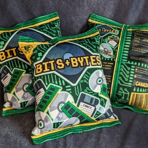 May include: Three green and yellow pillow-shaped chip bags with the text "Bits + Bytes" and a circuit board design. The bags are filled with a snack.
