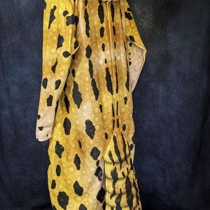 Puede incluir: Un disfraz de animal de cuerpo entero, de color amarillo y negro, con estampado de leopardo y capucha. La capucha tiene una cabeza de leopardo grande, de aspecto realista, de color amarillo y negro, con ojos negros.