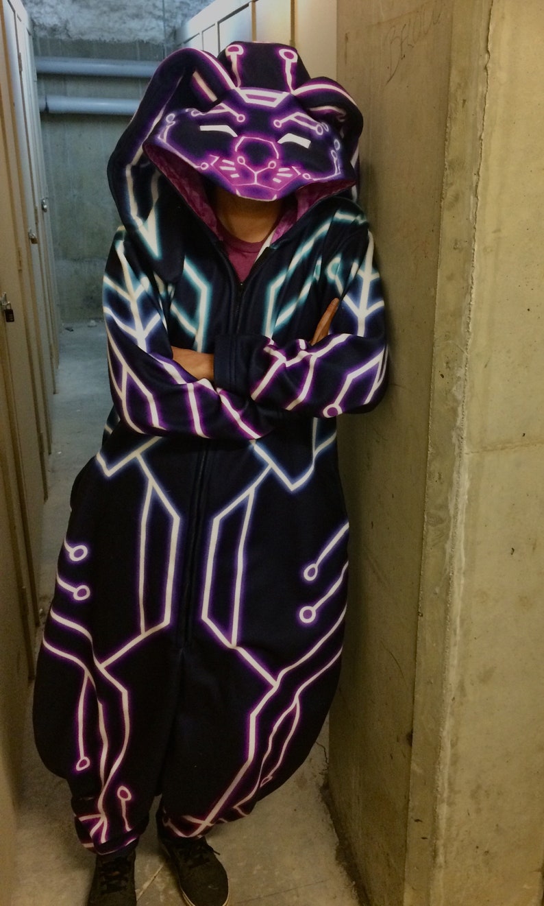 May include: A black hooded jumpsuit with a neon purple and white geometric pattern. The hood has a cat face design with neon purple and white details.