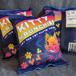 May include: Three blue and yellow pillow covers with the text "Kitty Krunchies Let the cat outta the bag" and a cartoon cat with a winking eye.