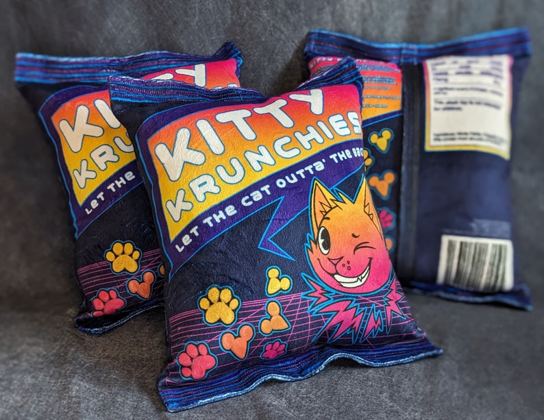 May include: Three blue and yellow pillow covers with the text "Kitty Krunchies Let the cat outta the bag" and a cartoon cat with a winking eye.