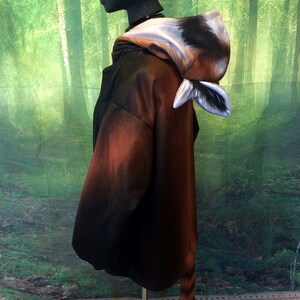 Puede incluir: Una sudadera marr&oacute;n y negra con un dise&ntilde;o de panda rojo. La sudadera tiene una capucha con una cabeza de panda rojo y una cola que cuelga de la espalda. La sudadera est&aacute; en un maniqu&iacute; contra un fondo de bosque verde.