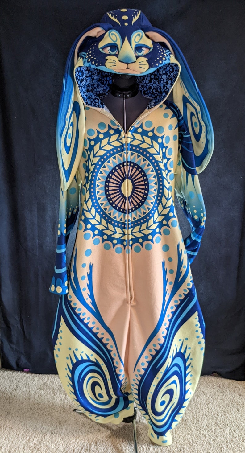 May include: A blue and yellow patterned hooded jumpsuit with a zipper closure and a bunny rabbit head design on the hood.