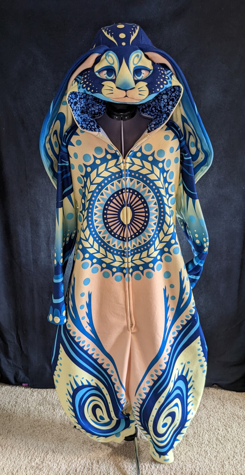 May include: A blue and yellow patterned hooded jumpsuit with a bunny head design. The hood has a zipper closure and the jumpsuit has a full-length zipper.
