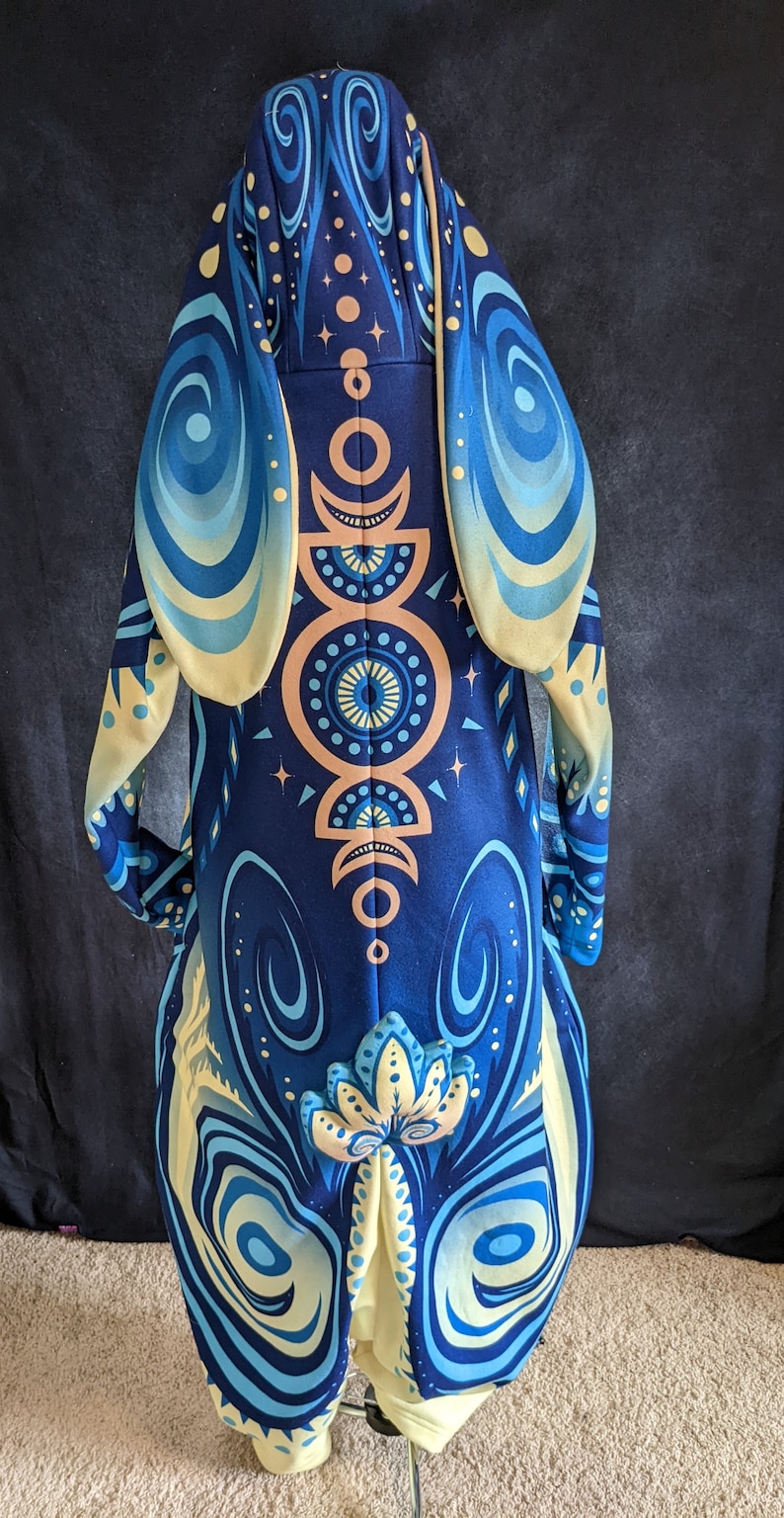 May include: A blue and yellow hooded jumpsuit with a moon and star pattern. The hood has large, floppy ears.