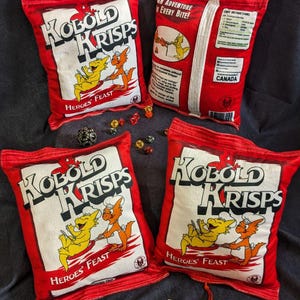 May include: Four red and white pillow-shaped chip bags with the words "Kobold Krisps" and "Heroes' Feast" printed on them. The bags are surrounded by dice and a red pouch.