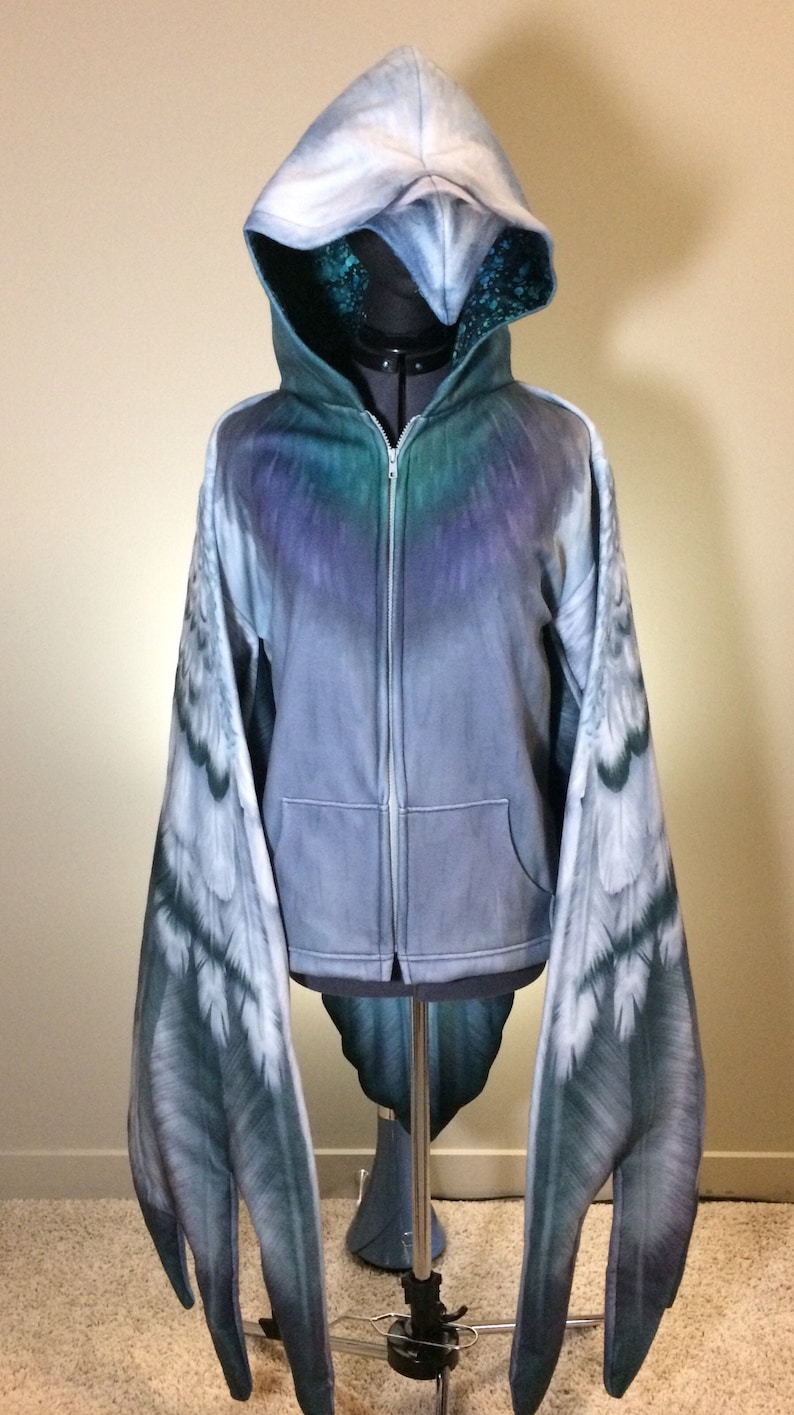 Puede incluir: Una sudadera con capucha azul y gris con cierre de cremallera y mangas largas. Las mangas est&aacute;n dise&ntilde;adas para parecer alas con un patr&oacute;n de plumas blancas y grises.